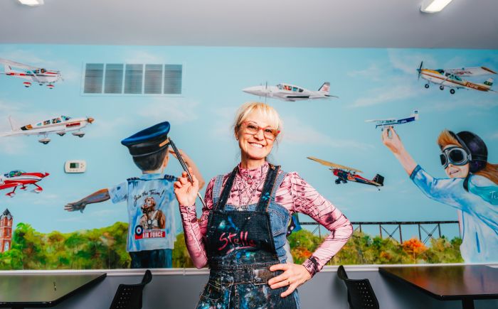 Stella Jurgen stands in front of her hand-painted airport in the Tillsonburg Regional Airport SkyWay Café Lounge